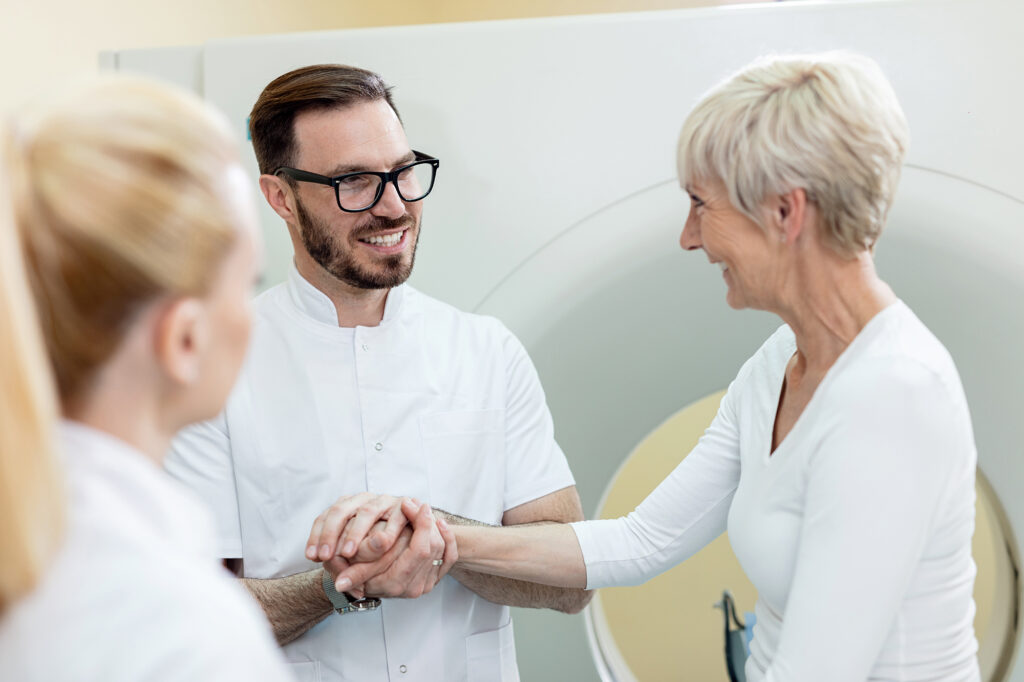 Happy doctor communicating with female patient and supporting her before CT scan examination in the hospital.